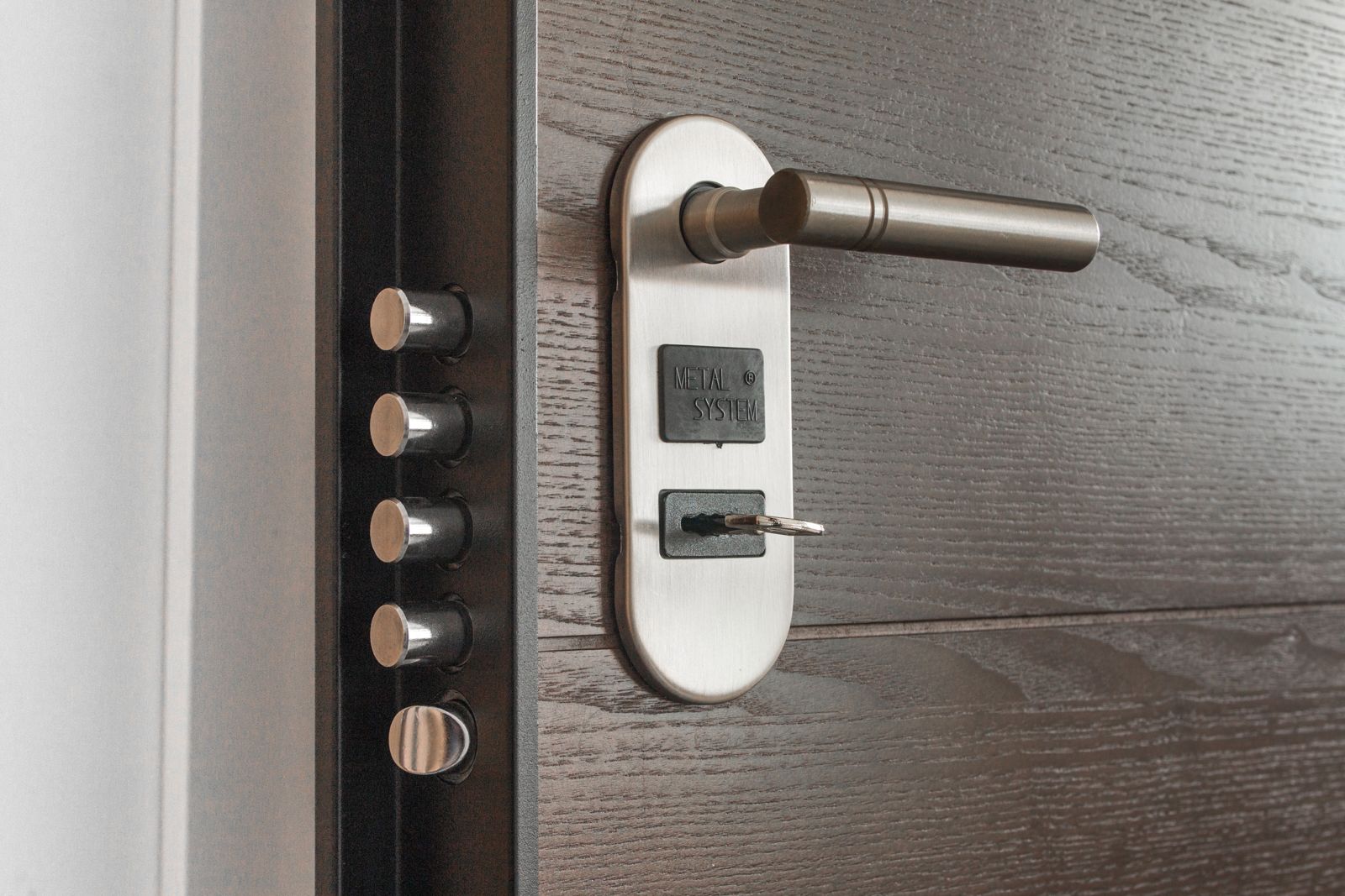 Security door edge with four round bolts and a key inserted in a steel handle plate