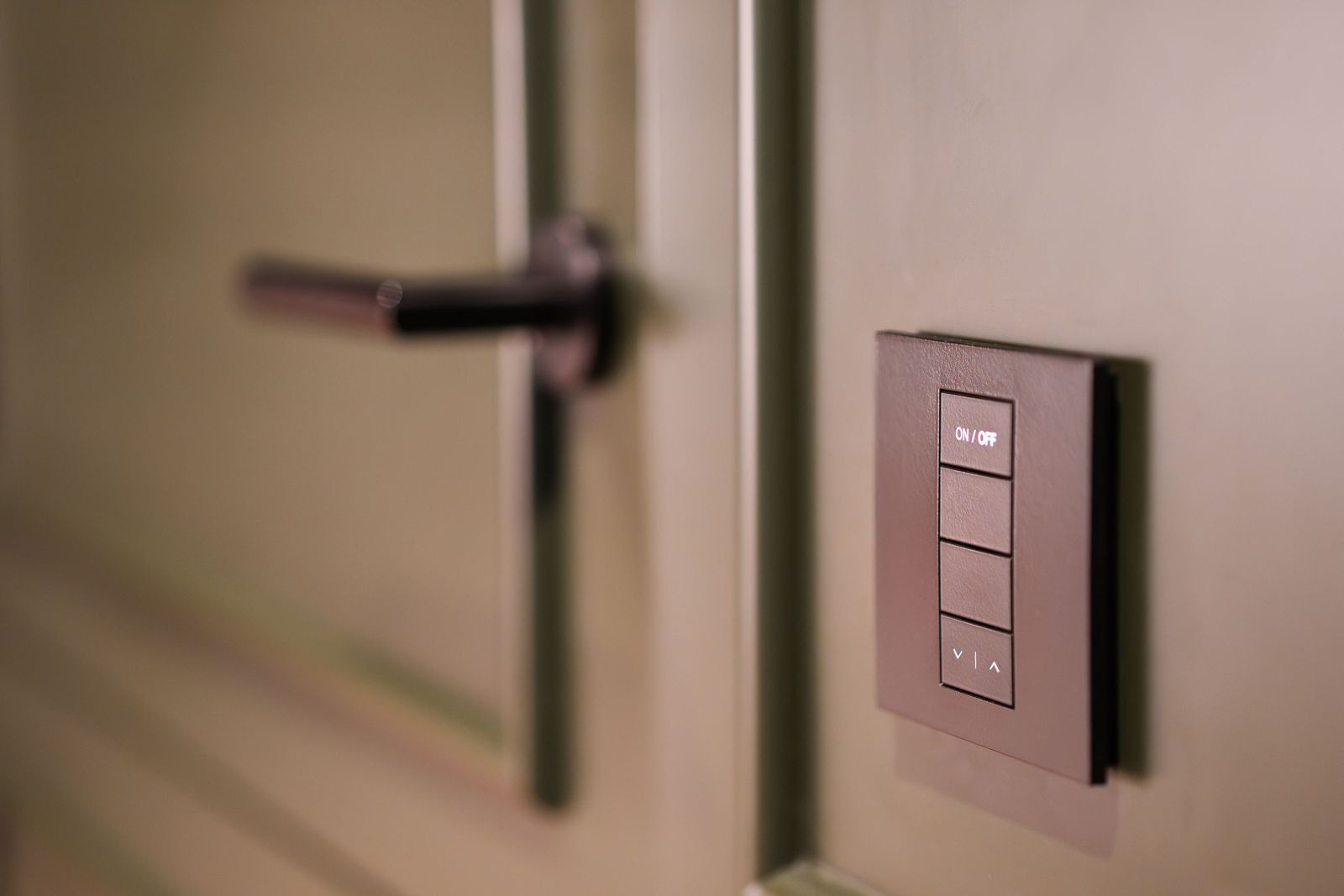 Slim bronze-tone wall control panel with on/off and up/down buttons next to a door handle